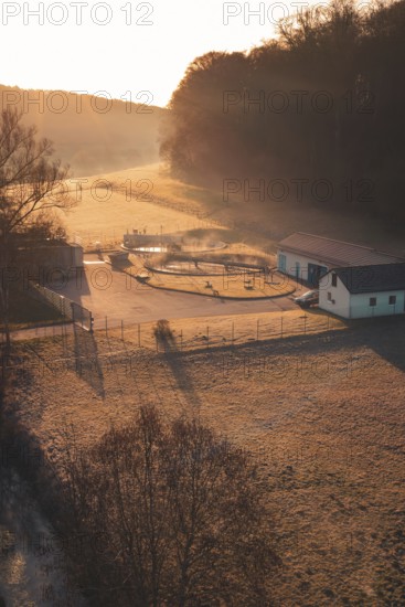 Sewage treatment plant at sunrise in a meadow with long shade, surrounded by trees and fog, Gechingen, Calw district, Germany