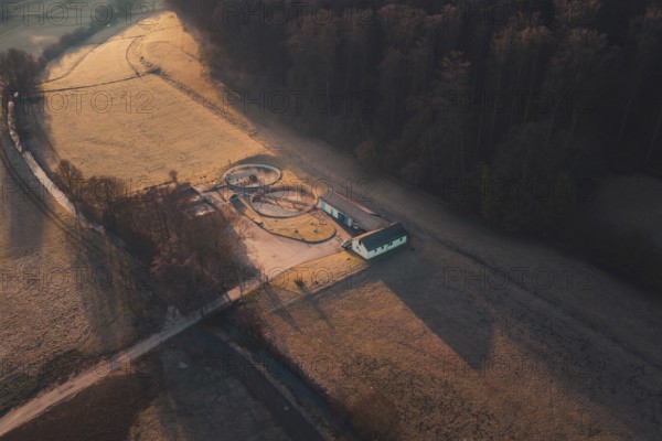 Wastewater treatment plant buildings and ornate paths in the middle of fields from a bird's eye view at sunrise, Gechingen, Calw district, Germany
