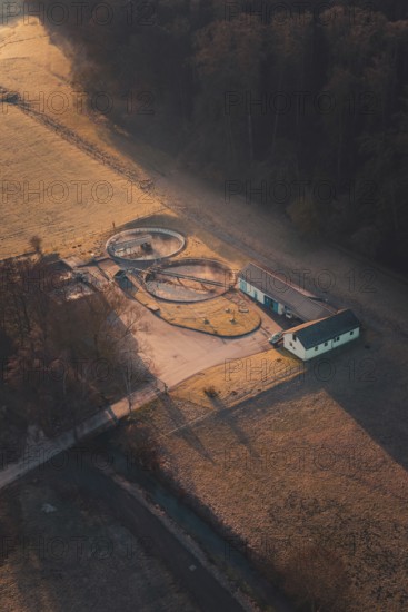 Sewage treatment plant surrounded by fields and trees, illuminated by the morning sun with long shadows, Gechingen, Calw district, Germany