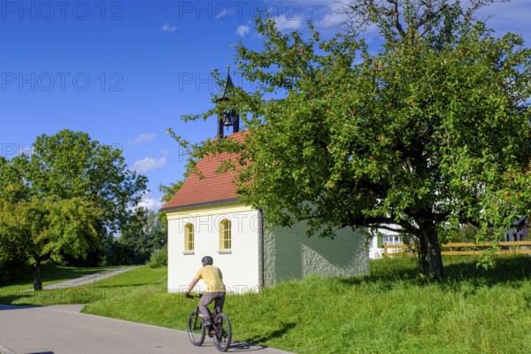 Cyclists in front of a chapel, Steingaden, near Sulzberg, Oberallgäu, Swabia, Bavaria, Germany