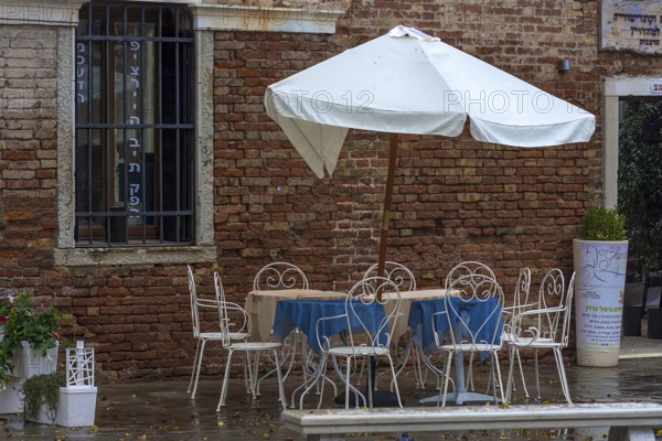 Empty seats with parasols in front of the Ghimel Garden kosher restaurant in Gheto Novo, Venice, Veneto, Italy