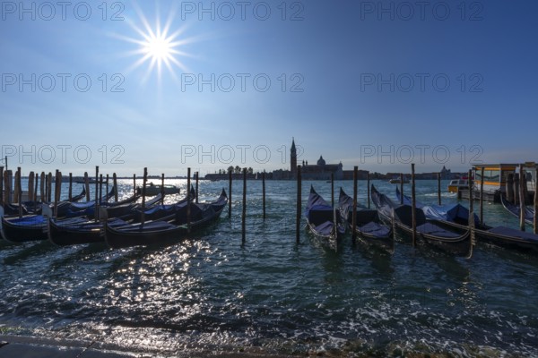 Gondolas at anchor, beginning floods, San Giorgio Maggiore church in the back, sun star, Venice, Veneto, Italy