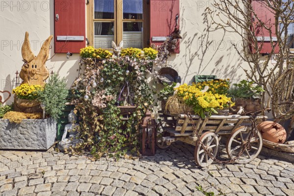 Easter decoration, wooden Easter bunny, historic handcart, flower pots, plant pots, plant pots, house, façade with windows and shutters, street made of paving stones, sunny, Inzell, Traunstein district, Bavaria, Germany