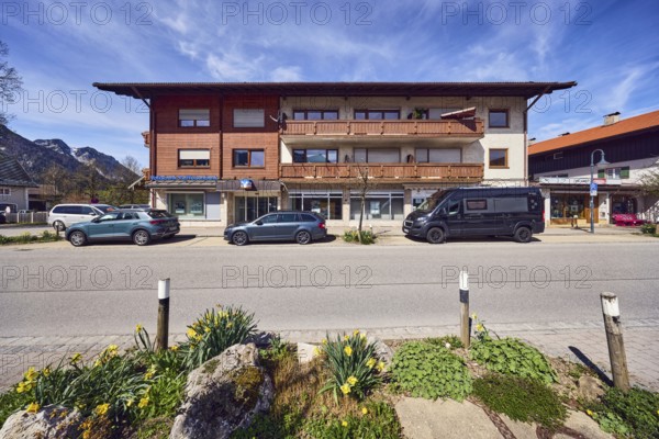 Volksbank Raiffeisenbank Oberbayern Südost eG, residential and commercial buildings, alpine buildings, façade with windows and balcony, building material wood, parking strips with cars, barrier bollard, flower bed, mountain, blue sky, cirrus clouds, cirrostratus clouds, Traunsteiner Straße, Inzell, district of Traunstein, Bavaria, Germany