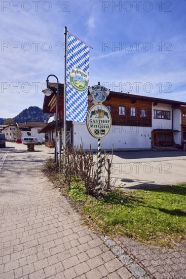 Privatbrauerei Ayinger, advertising flag on flagpole, Hirschbichler inn and butcher shop, commercial building, alpine building, lantern, grass, bushes, back light, blue sky, cirrus clouds, cirrostratus clouds, Traunsteiner Straße, Inzell, Traunstein district, Bavaria, Germany