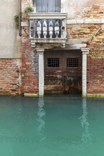 Dilapidated house façade with balcony and door on the canal during floods, Venice, Veneto, Italy