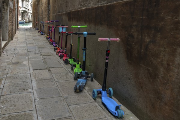 Parked colorful children's scooters, scooters on a wall in front of a kindergarten, Venice, Veneto, Italy