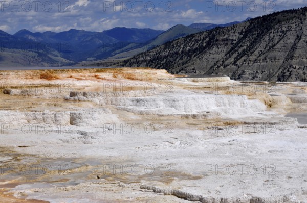 Limestone terraces against mountain backdrop under cloudy sky, Yellowstone National Park, Wyoming, USA