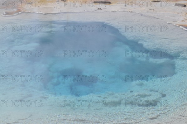 Blue hot spring surrounded by steam and natural geology, Yellowstone National Park, Wyoming, USA