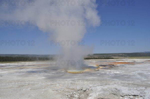 A hot spring with rising steam in an open landscape under clear skies, Yellowstone National Park, Wyoming, USA