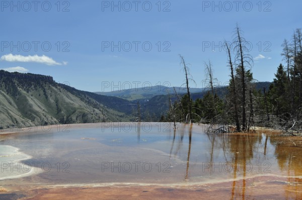 Natural pool with volcanic deposits and reflections and extensive views of mountains, Yellowstone National Park, Wyoming, USA