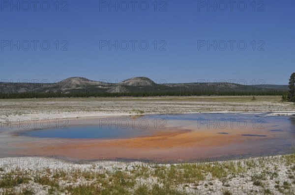 An orange geothermally active area in front of a mountainous landscape, Yellowstone National Park, Wyoming, USA