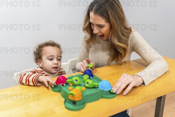 Happy mother and toddler play a colorful tabletop turtle game, smiling and learning together while bonding, exploring skills, concentration, and joyful discovery at home