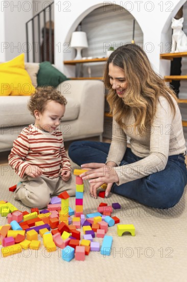 Mother and young son are sitting on the floor at home, building a tower with vibrant wooden blocks, enjoying a moment of playful interaction and early childhood development
