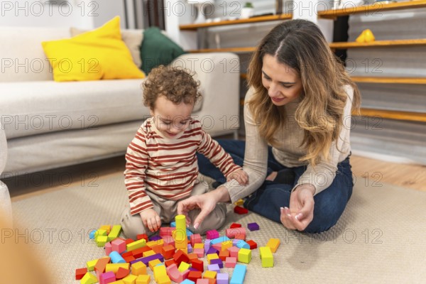 Loving mother and her smiling toddler son are sitting on the floor at home, engaging in creative play with colorful wooden building blocks, fostering developing skills and early childhood learning