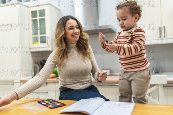 Mother and young child bonding over a coloring book and watercolor palette on a kitchen table, sharing a happy moment of learning and artistic expression