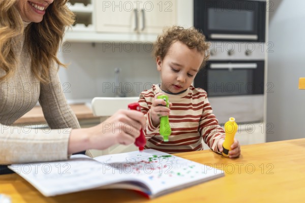 Young child and mother engaging in a fun creative painting activity, using colorful paint dot markers in a coloring book at home, fostering early childhood education and family bonding