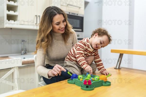 Happy mother and her toddler son enjoying a fun board game together at the kitchen table, sharing laughter and creating a positive family bonding experience indoors