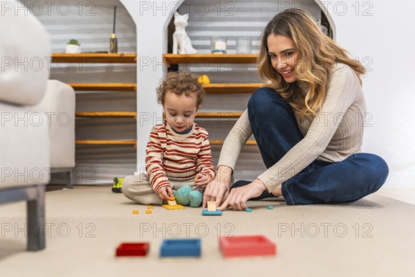 Young mother happily interacting with her toddler son, both sitting on a carpeted floor, engrossed in playing and learning with colorful educational building toys at home