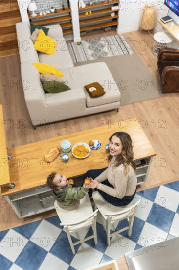 Happy mother and toddler boy sharing a morning meal at a kitchen island, creating a tender moment of family togetherness and domestic life from an overhead view
