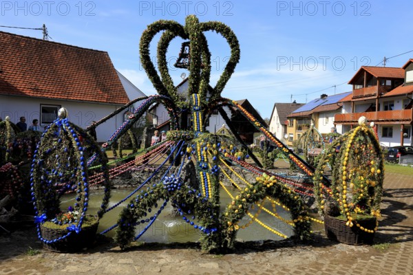 Easter fountain in Bieberbach, supposedly the largest Easter fountain in the world, Egloffstein market, Franconian Switzerland, Forchheim district, Upper Franconia, Bavaria, Germany, lavishly decorated Easter fountain in the village square, surrounded by farmhouses under a blue sky