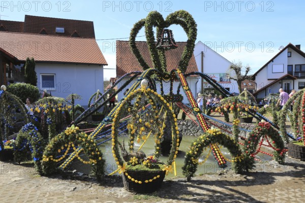 Easter fountain in Bieberbach, supposedly the largest Easter fountain in the world, Egloffstein market, Franconian Switzerland, Forchheim district, Upper Franconia, Bavaria, Germany, festively decorated fountain with colorful Easter elements, cheerful atmosphere in the sunny village