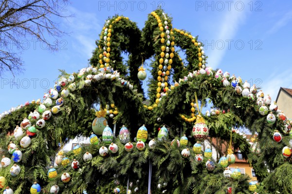 Easter fountain in Heiligenstadt, Franconian Switzerland, Bamberg district, Upper Franconia, Bavaria, Germany, An Easter fountain decorated with numerous colorful eggs against a clear, blue sky in a historic setting