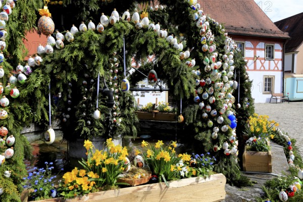 Easter fountain in Heiligenstadt, Franconian Switzerland, Bamberg district, Upper Franconia, Bavaria, Germany, A richly decorated Easter fountain with painted eggs and yellow flowers in front of a historic building