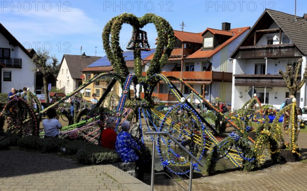 Easter fountain in Bieberbach, supposedly the largest Easter fountain in the world, Egloffstein market, Franconian Switzerland, Forchheim district, Upper Franconia, Bavaria, Germany, heart-shaped fountain made of Easter eggs and spruce branches in a village environment