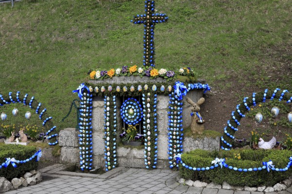 Easter fountain in Tiefenpölz, Heiligenstadt market, Franconian Switzerland, Bamberg district, Upper Franconia, Bavaria, Germany, Easter fountain with colorful decorations and a cross in a green setting