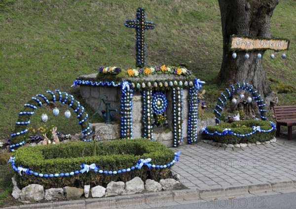 Easter fountain in Tiefenpölz, Markt Heiligenstadt, Franconian Switzerland, Bamberg district, Upper Franconia, Bavaria, Germany, decorative Easter fountain with a cross next to a tree and a bench