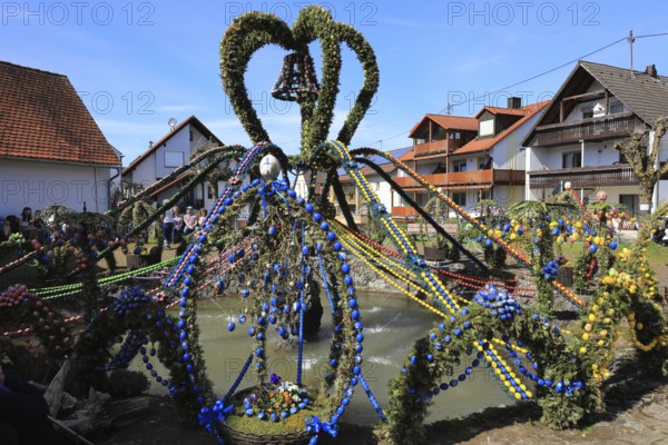 Easter fountain in Bieberbach, supposedly the largest Easter fountain in the world, Egloffstein market, Franconian Switzerland, Forchheim district, Upper Franconia, Bavaria, Germany, lavishly decorated Easter fountain with colorful garlands in a village under a clear, sunny sky