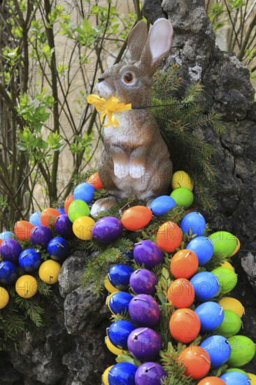 Easter fountain in Franconian Switzerland, Bamberg district, Upper Franconia, Bavaria, Germany, Easter bunny with yellow ribbon surrounded by colorful Easter eggs in natural surroundings