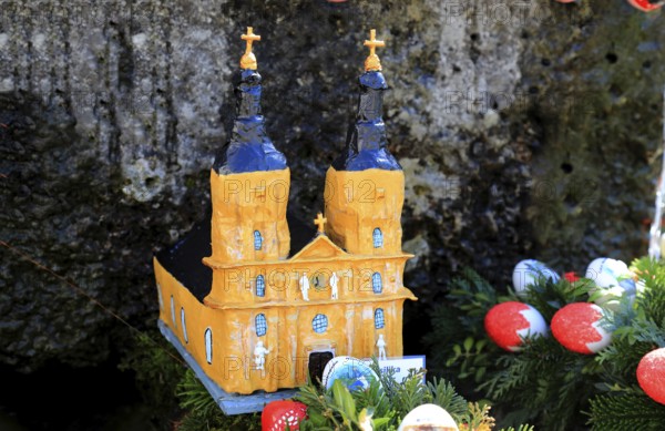 The monastery church Vierzehnheiligen as a model built into an Easter fountain, Franconian Switzerland, in Kleingesee, Gößweinstein market in the district of Forchheim, Upper Franconia, Bavaria, Germany, yellow church model with surrounding Easter eggs and green branches, festive atmosphere