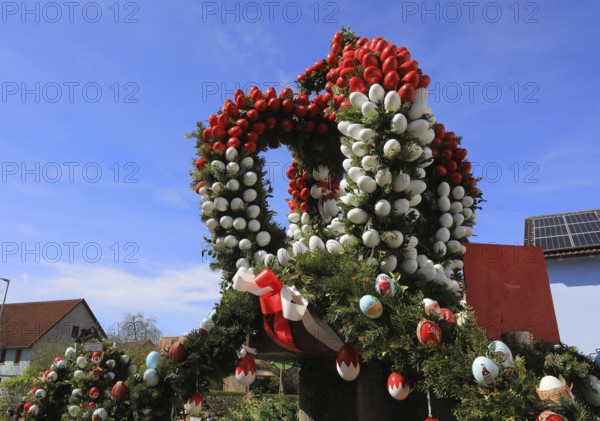 Detail of an Easter fountain in Franconian colors red and white, Franconian Switzerland, in Kleingesee, Gößweinstein market in the district of Forchheim, Upper Franconia, Bavaria, Germany, decorative structure with Easter eggs and spruce branches between residential buildings, blue sky