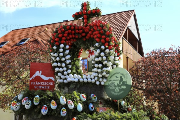Detail of an Easter fountain in Franconian colors red and white, Franconian Switzerland, in Kleingesee, Gößweinstein market in the district of Forchheim, Upper Franconia, Bavaria, Germany, decorative Easter crown with flowers and wreaths, represents the Franconian Switzerland region against a blue sky