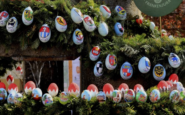 Detail of an Easter fountain in Franconian colors red and white, eggs with coats of arms of the surrounding communities, Franconian Switzerland, in Kleingesee, Gößweinstein market in the district of Forchheim, Upper Franconia, Bavaria, Germany, detailed Easter eggs on spruce branches with regional coats of arms