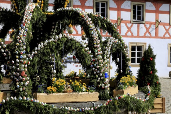 Easter fountain in Heiligenstadt, Franconian Switzerland, Bamberg district, Upper Franconia, Bavaria, Germany, An Easter fountain with numerous colorful eggs and flower decorations in front of a traditional house