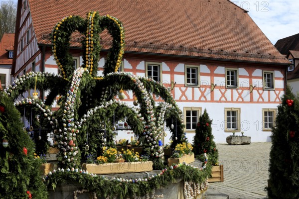 Easter fountain in Heiligenstadt, Franconian Switzerland, Bamberg district, Upper Franconia, Bavaria, Germany, A festively decorated Easter fountain with hand-painted eggs in front of a traditional half-timbered house under a blue sky