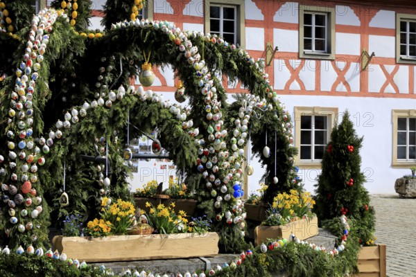 Easter fountain in Heiligenstadt, Franconian Switzerland, Bamberg district, Upper Franconia, Bavaria, Germany, detail of an Easter fountain decoration with colorful, hand-painted eggs and flowers in front of a half-timbered house