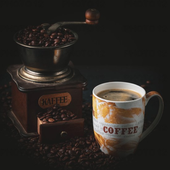 Coffee grinder next to a cup with coffee and beans on a dark background