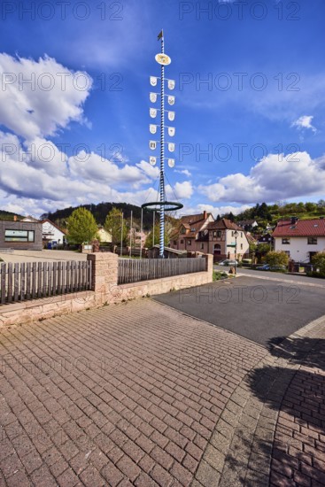 Maypole, sandstone wall, wooden fence, roads, general buildings, residential buildings, hills, coniferous forest, blue sky, cumulus clouds, confluence of Hessenthälchenweg in Am Mühlbach, Waldaschaff, Lower Franconia, Aschaffenburg district, Bavaria, Germany