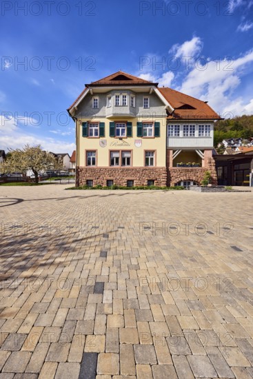 Town hall, commercial building, façade with windows, shutters and façade painting, hipped roof, general development, paving brick walkway, hill, coniferous forest, blooming tree, blue sky, cumulus clouds, cirrus clouds, Am Mühlbach, Waldaschaff, Lower Franconia, Aschaffenburg district, Bavaria, Germany