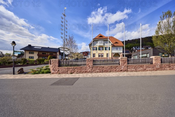 Town hall, maypole, flagpoles, lantern, sandstone wall, wooden fence, street, general development, commercial building, residential development, hill, coniferous forest, blue sky, cumulus clouds, cirrus clouds, confluence Hessenthälchenweg in Am Mühlbach, Waldaschaff, Lower Franconia, Aschaffenburg district, Bavaria, Germany