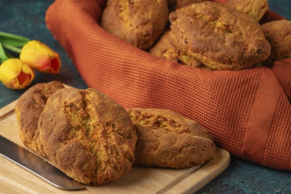 Fresh potato rolls in a basket with orange cloth, some on a wooden board