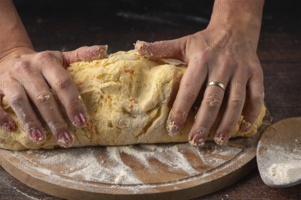 Hands knead a large lump of dough on a floured wooden board