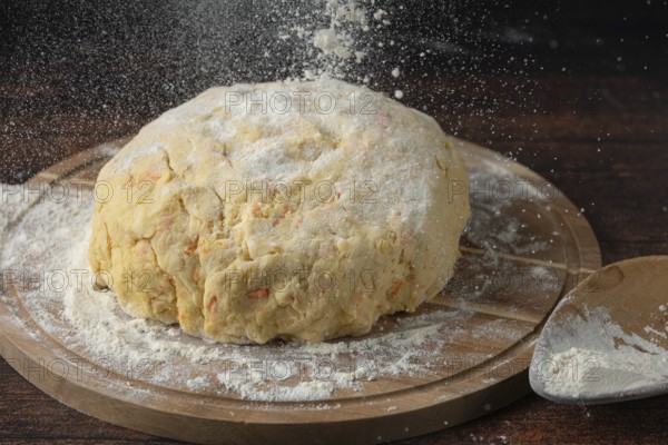 Dough is sprinkled with flour on a wooden board