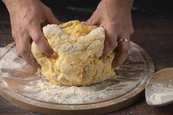 Two hands knead dough on a floured wooden board in the kitchen