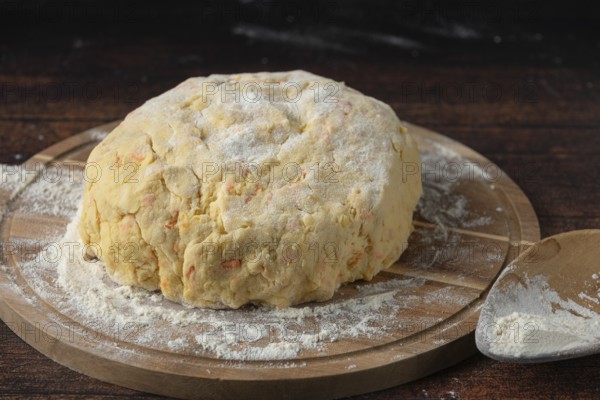 A lump of dough covered with flour on a wooden board in a dark kitchen