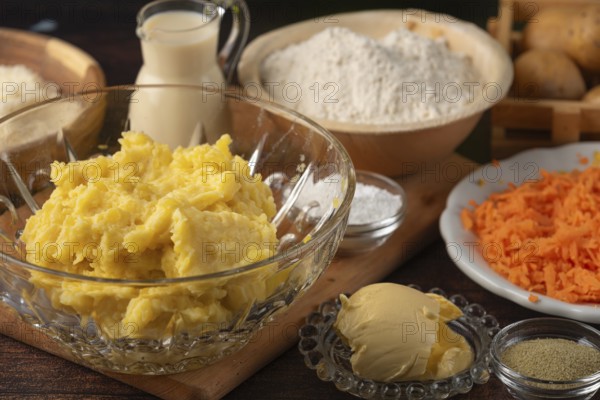 Mashed potatoes and grated carrots next to flour and milk on a wooden table